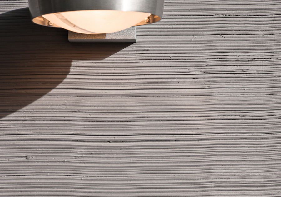 Nahaufnahme einer strukturierten Wandoberfläche mit Lichtspiel unter Wandlampe