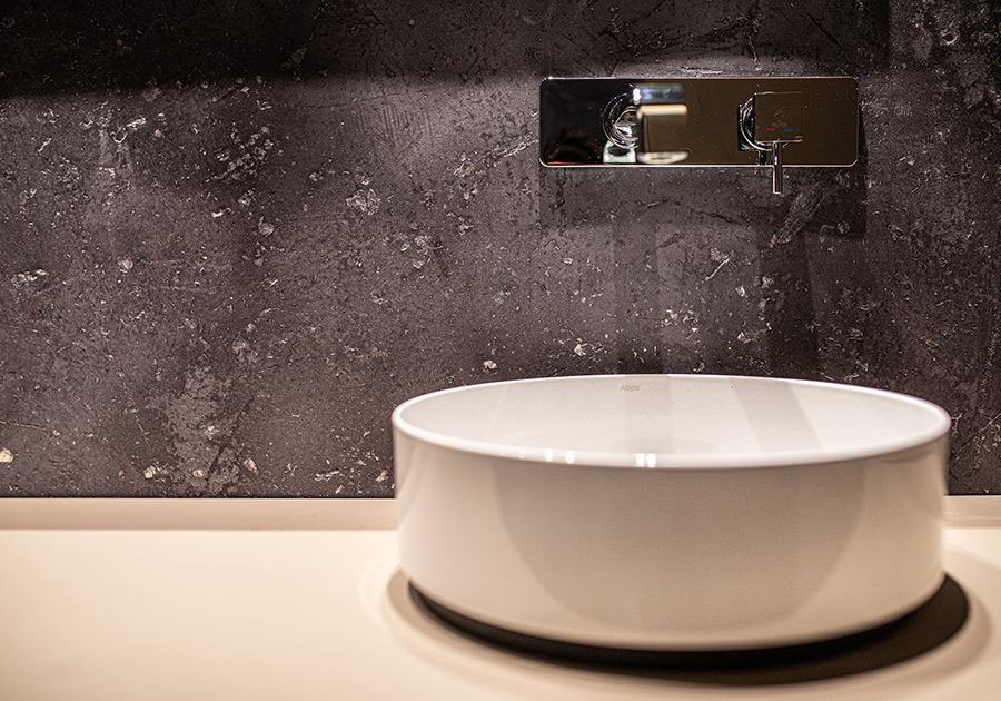 Rundes, weißes Waschbecken vor einer strukturreichen, dunklen Wandfläche
