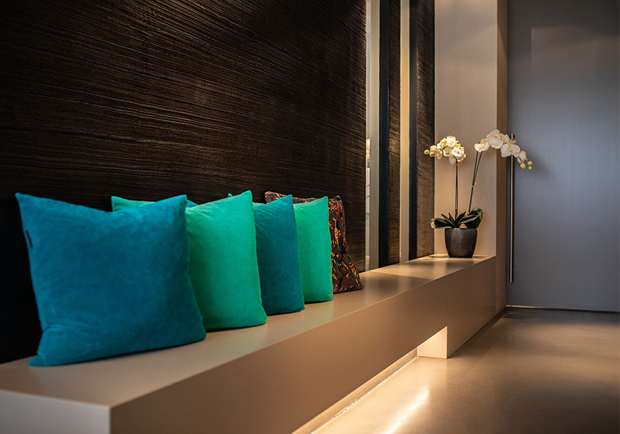 Sitzbank mit türkisfarbenen Kissen vor strukturierter, dunkler Wand